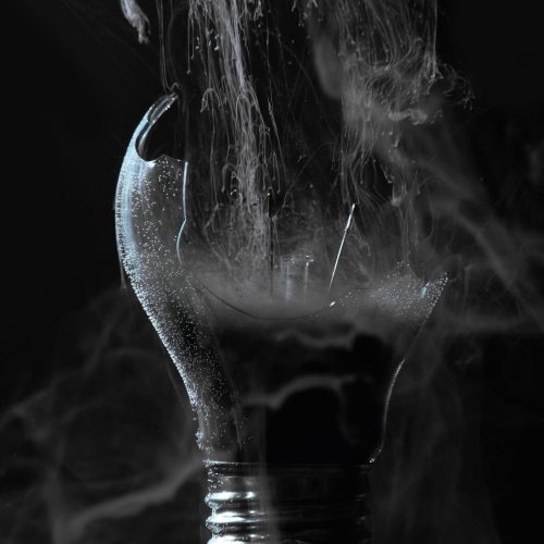 Lamp explosion smoke cloud. Power failure. Defocused gray color vapor haze in broken glass light bulb on dark black night abstract background.